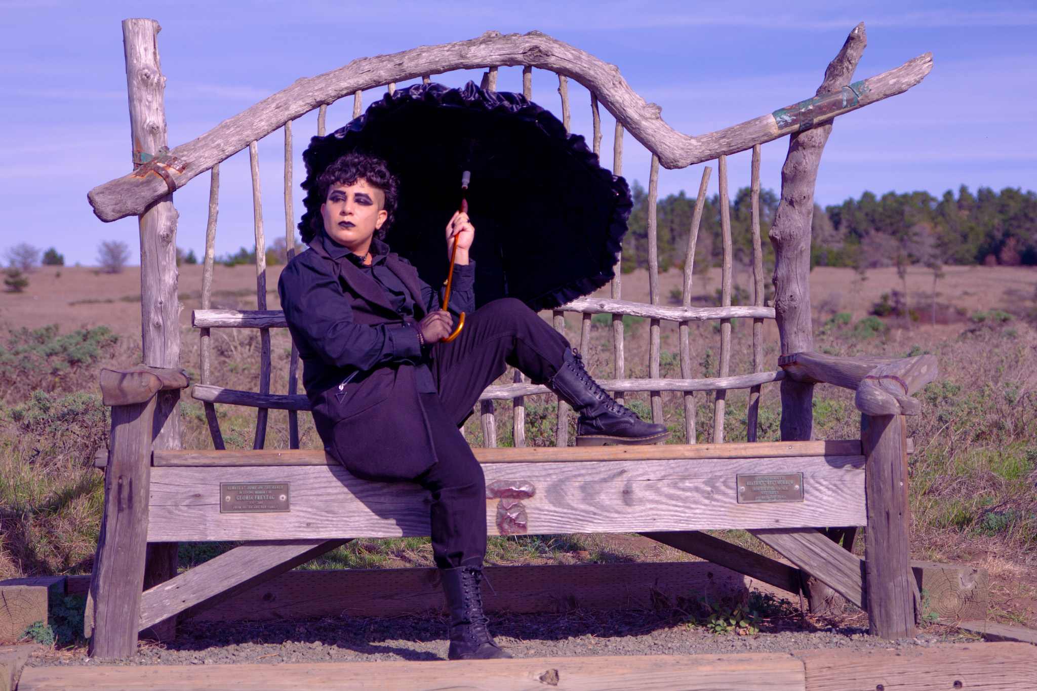 Me in all black, holding a lacy umbrella, sitting on an old wooden bench along the seaside in Cambria